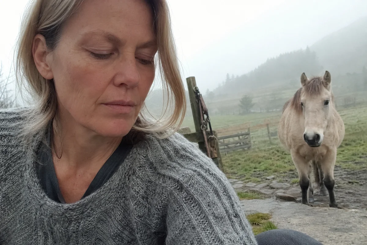 Close, quiet moment, a person breathing slowly while a horse stands nearby in a misty paddock